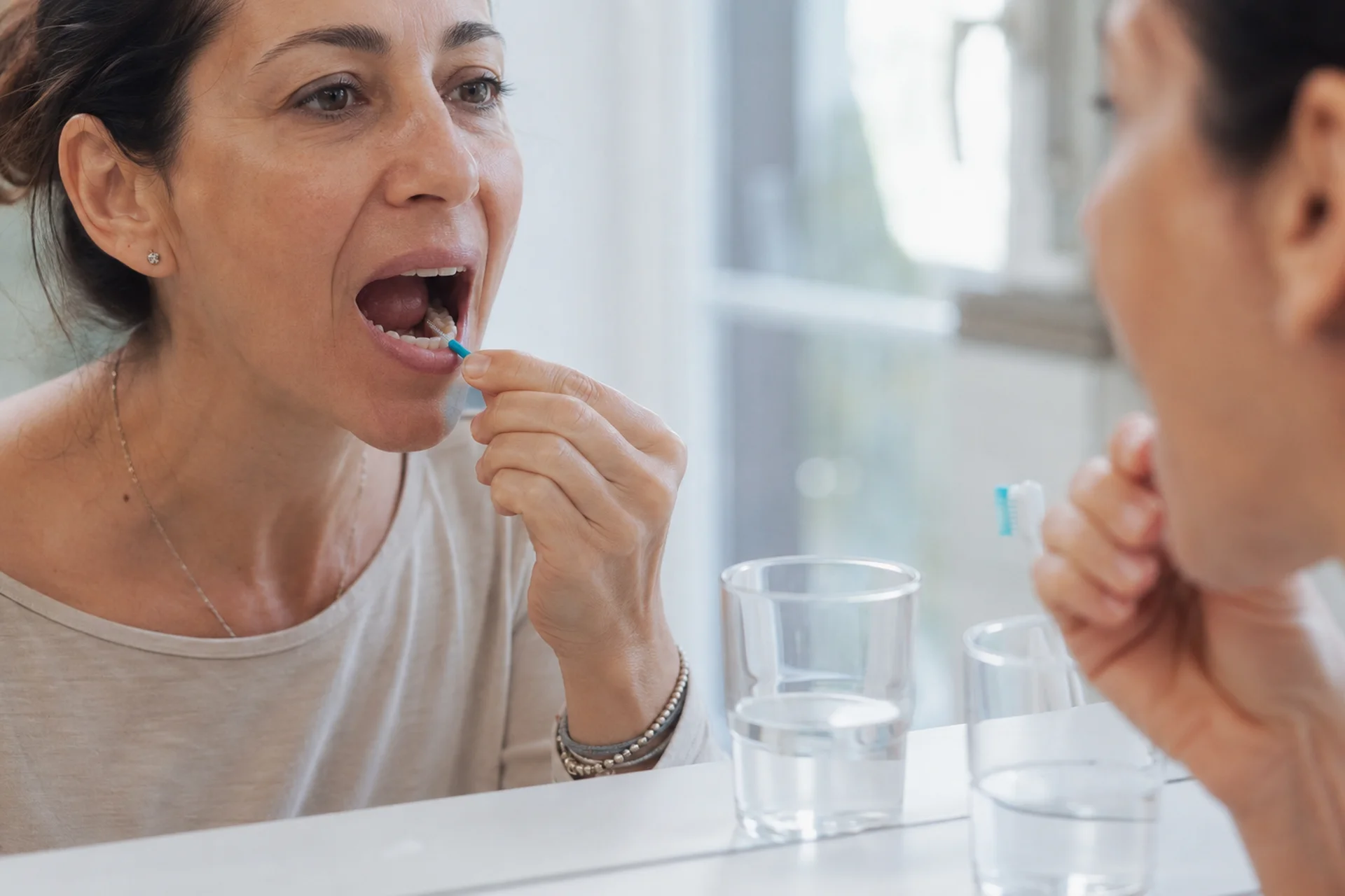 Donna che usa lo scovolino interdentale attorno a un impianto dentale durante la routine di igiene quotidiana